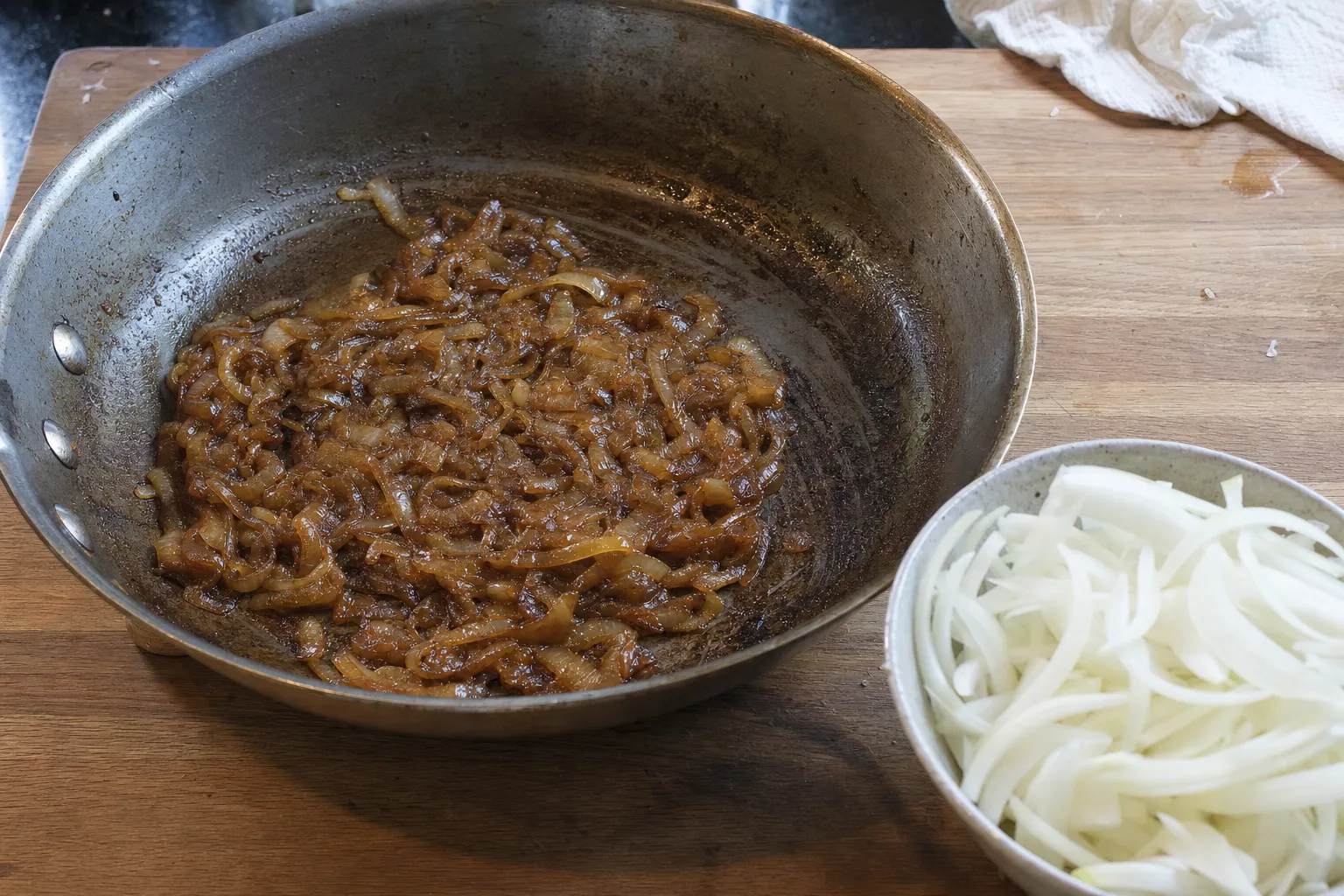 フライパンでじっくり炒めて濃い茶色になった玉ねぎと、器に入った炒める前の薄切り玉ねぎ