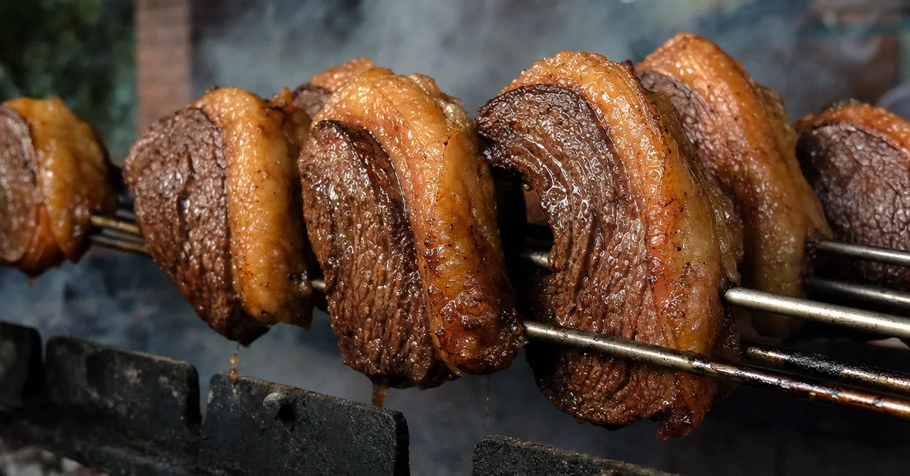 脂を外側にしてC字形に曲げたピッカーニャを串に刺し、焼き台の上で煙を上げて焼いている様子